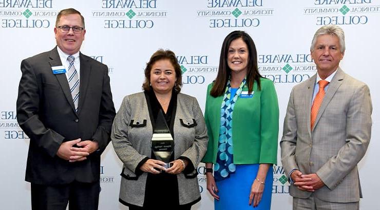 Mark Brainard, Lora Johnson, Yvette Santiago, and Daniel Ehmann stand in a line in front of a Delaware Tech backdrop with Yvette Santiago holding the Hispanic Heritage Month Honoree Award